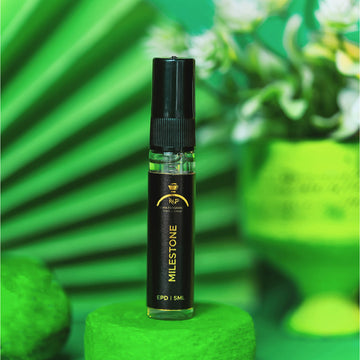 Milestone vape pen on a green pedestal with a green background and flowers.