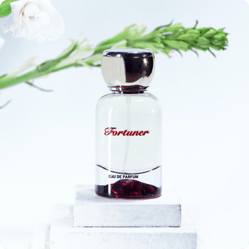 Perfume bottle labeled 'Fortuner' on a white background with greenery.